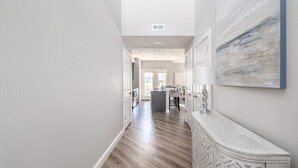 A hallway with a wooden floor, a white wall with a geometric pattern, and a ceiling vent. - Relax in Style, Golf course Community Townhouse - 3440 (Baldwinsville)