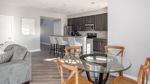 A modern kitchen with dark cabinets, a stainless steel refrigerator, and a microwave. There is a glass dining table with wooden chairs. - Relax in Style, Golf course Community Townhouse - 3440 (Baldwinsville)