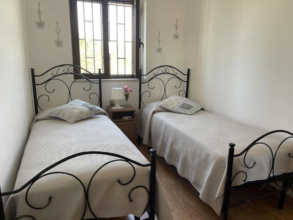 A bedroom with two single beds, a nightstand with a lamp and flowers, and a window with bars.