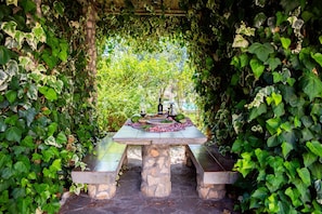 Un tavolo in pietra con un'attrezzatura da picnic in un giardino circondato dall'edera.