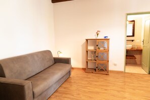 A living room with a grey sofa, a wooden bookshelf, and a door leading to a bathroom.