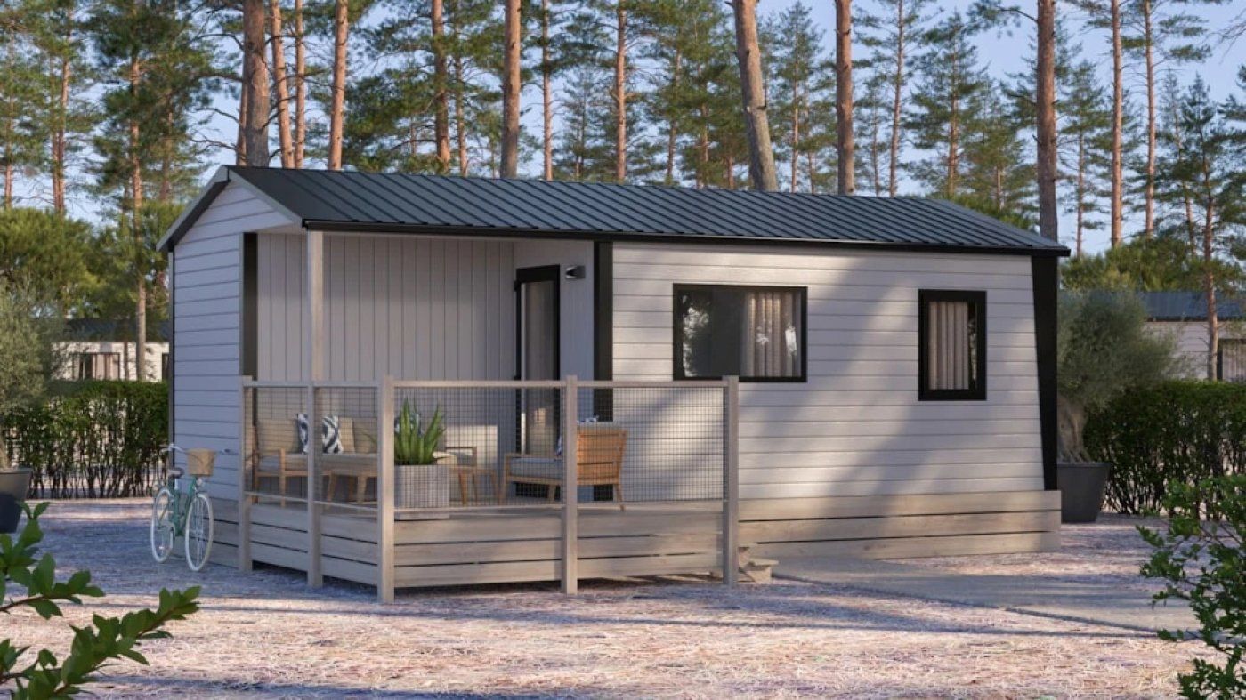 Une petite cabane en bois d’un seul étage, dotée d’un porche et entourée d’arbres.