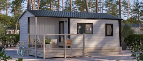 Une petite cabane en bois d’un seul étage, dotée d’un porche et entourée d’arbres.
