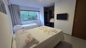 Habitación de hotel con cama, ventana con vista a zonas verdes, televisor montado en la pared y armario.