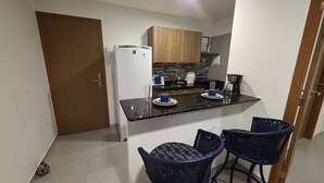 Una cocina compacta con refrigerador, cafetera y dos sillas de mimbre.