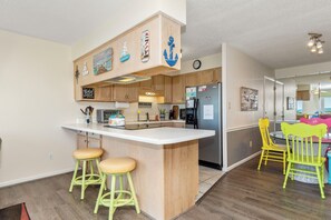 Eine Küche mit Holzschränken, einer zentralen Kochinsel mit Hockern, einem Kühlschrank und einem Essbereich mit Stühlen.