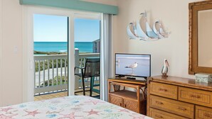 A bedroom with a balcony, a television, and a dresser. - Almost Oceanfront 3 Bedroom Pebble Beach C-304 Condo (Emerald Isle)