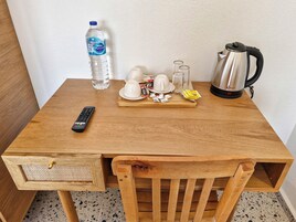 A wooden table with a remote control, a water bottle, a coffee maker, and a tray with cups and snacks.