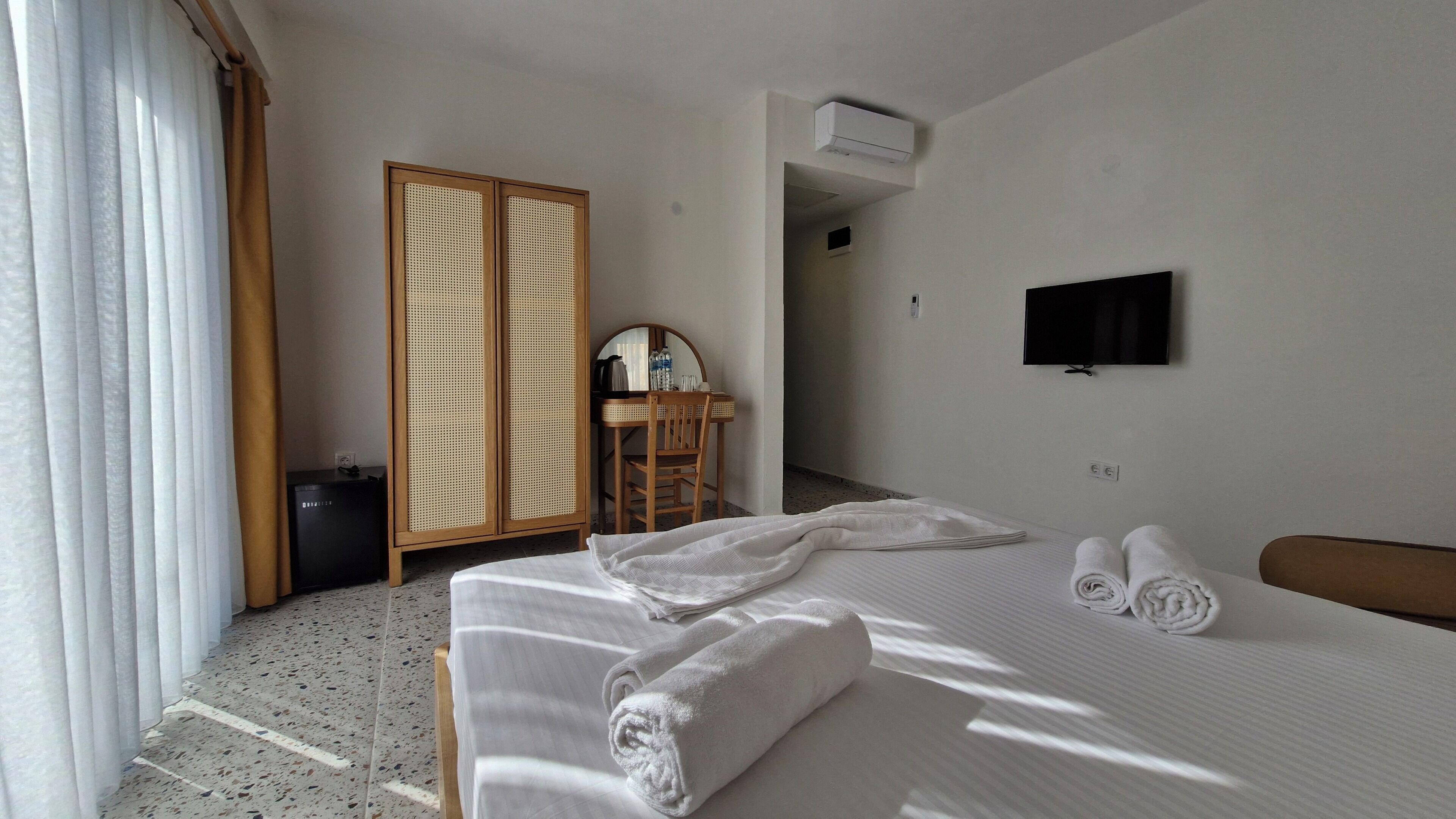 Habitación de hotel con cama, escritorio, silla, armario y televisor en la pared.