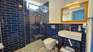 Une salle de bain avec des carreaux bleu foncé, un lavabo blanc, un miroir et un espace douche.