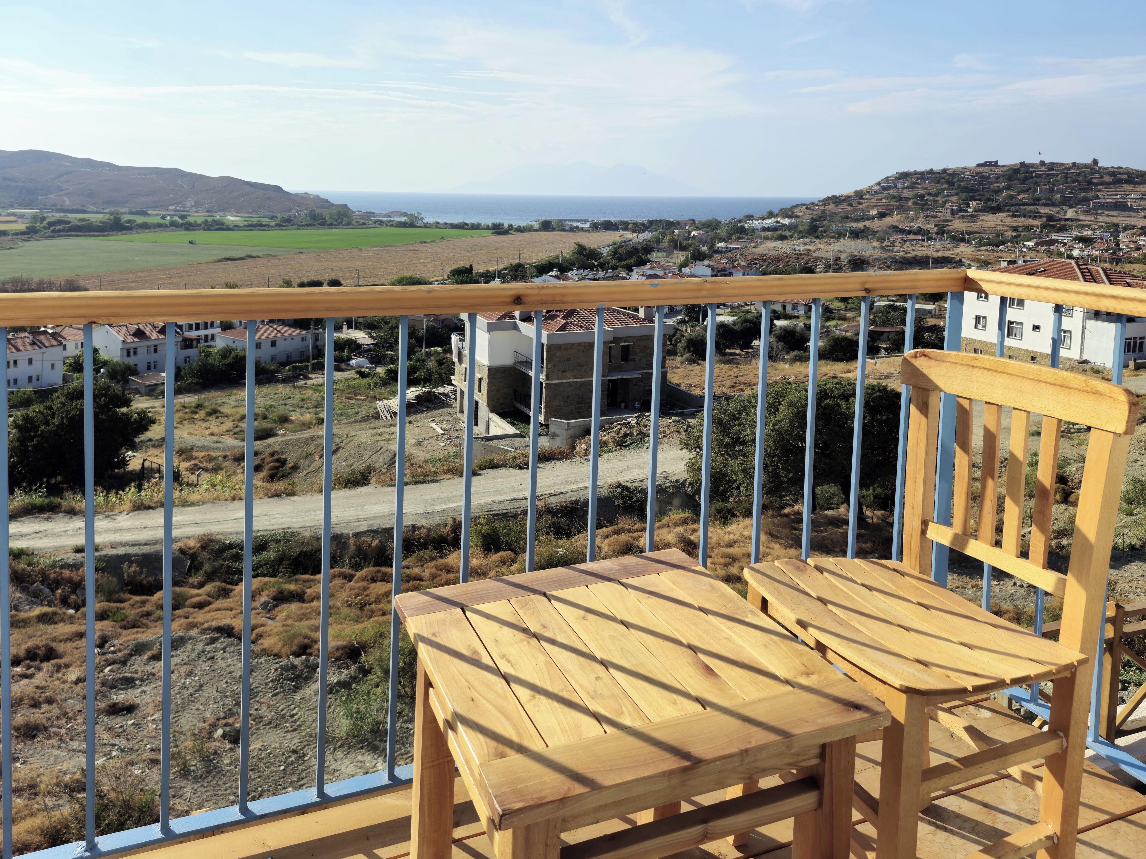 Terraza de madera con una silla, con vistas a un paisaje rural que incluye campos, una carretera y edificios a lo lejos.