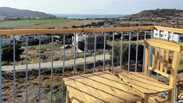Terraza de madera con una silla, con vistas a un paisaje rural que incluye campos, una carretera y edificios a lo lejos.