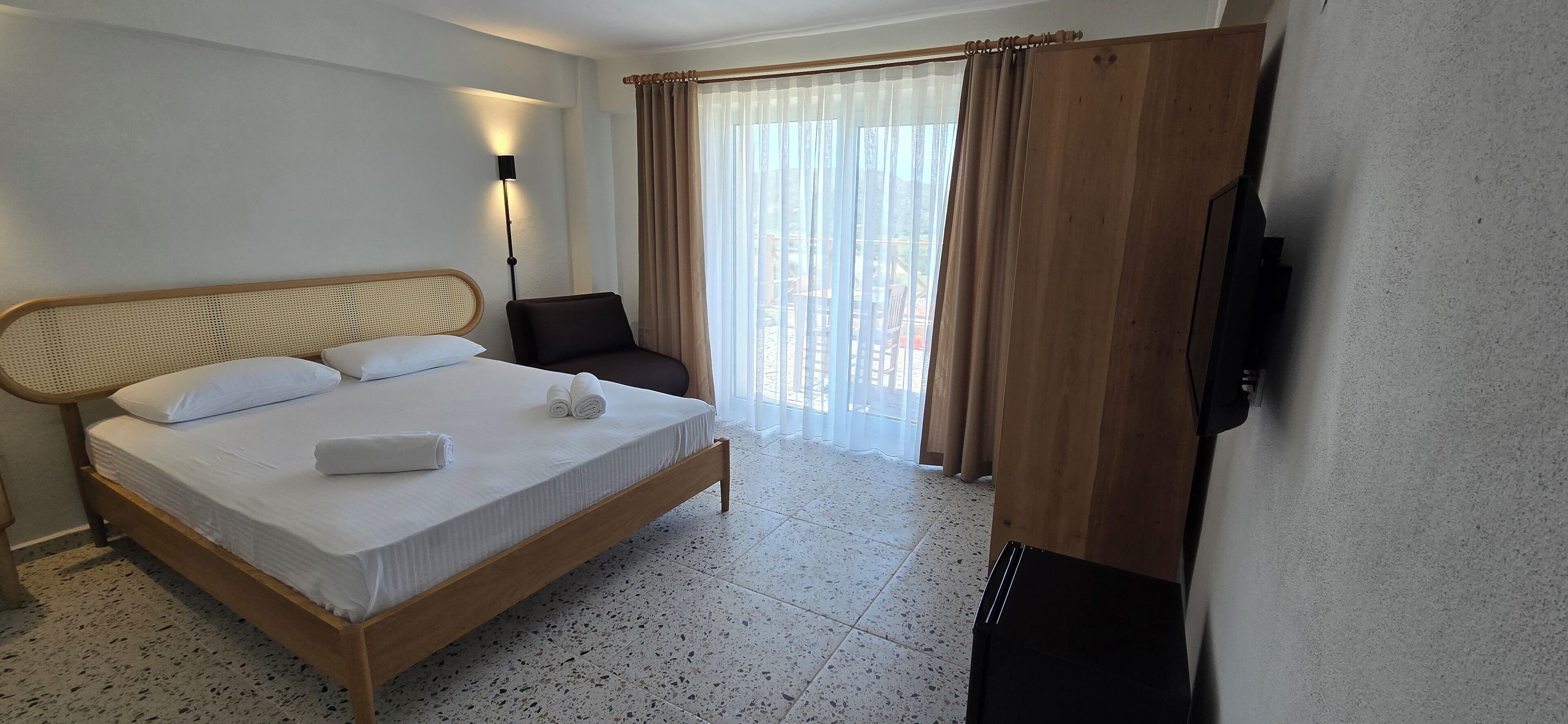 A hotel room with a bed, a chair, a TV, and a window with curtains.
