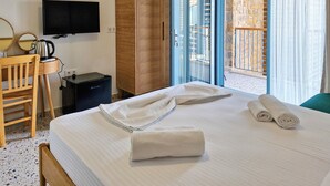 Une chambre d’hôtel comprenant un lit, une armoire en bois, un bureau avec une bouilloire, une télévision et un balcon doté d’un mur en pierre.
