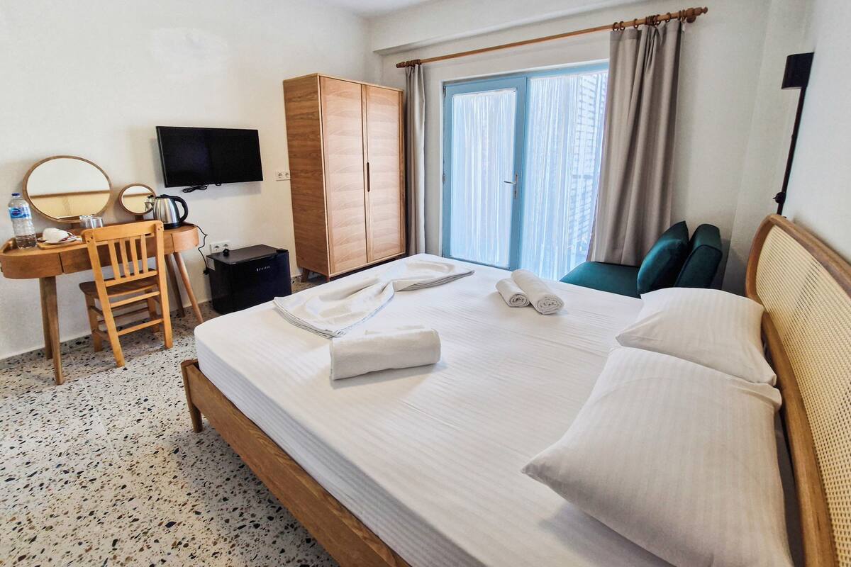A hotel room with a bed, a desk with a chair, a wardrobe, a television, and a window with curtains.