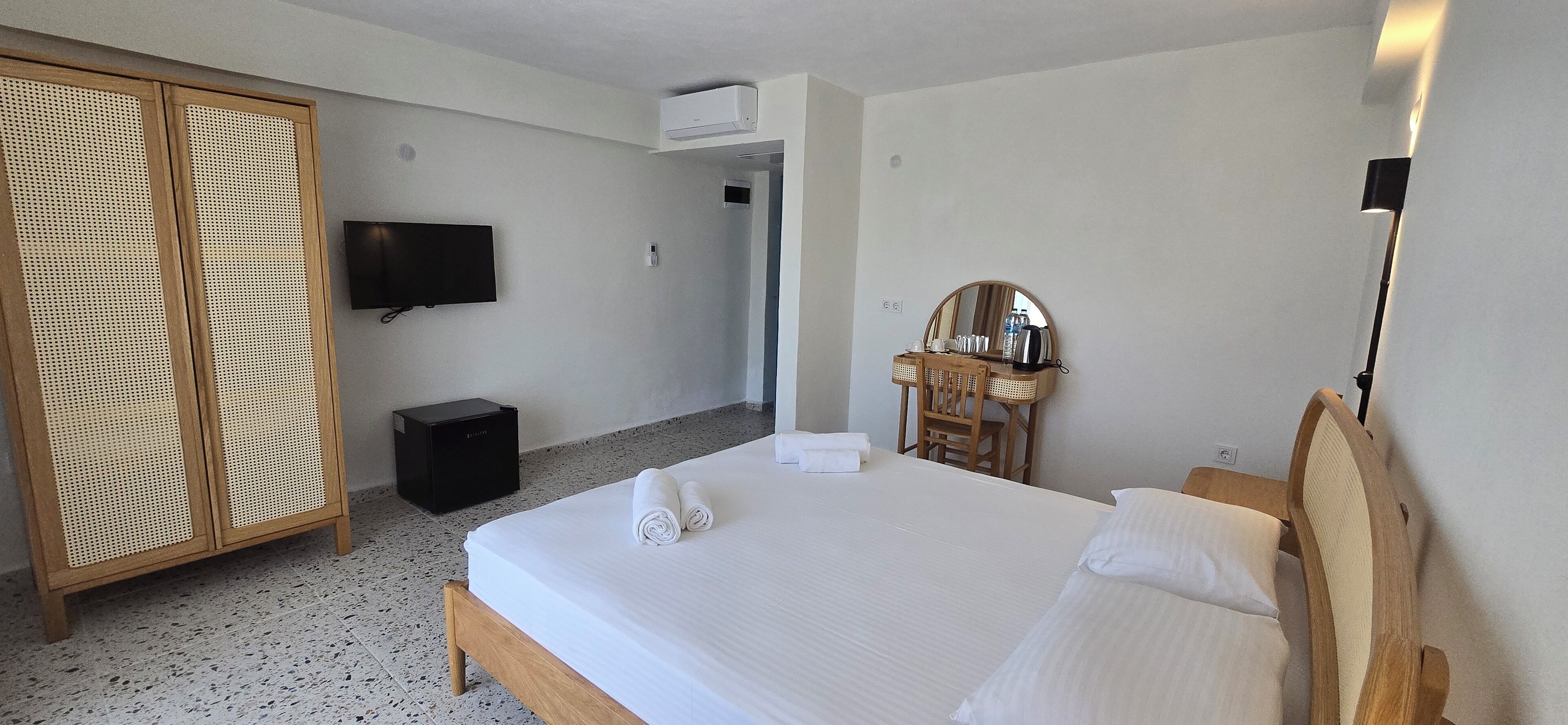 Habitación de hotel con cama, televisor, armario, escritorio con espejo y un taburete pequeño.