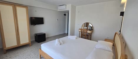 Habitación de hotel con cama, televisor, armario, escritorio con espejo y un taburete pequeño.