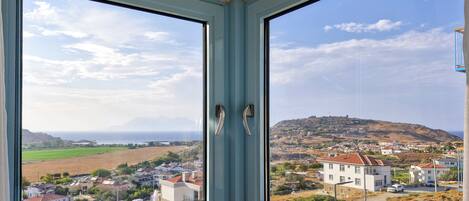 A corner room with two large windows offering a view of a coastal town and hills.