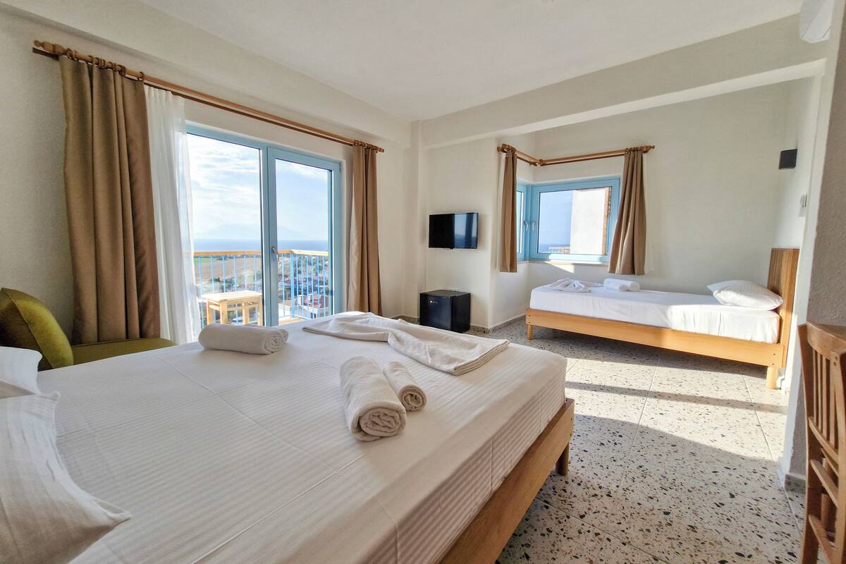A hotel room with a large bed, a smaller bed, a TV, and a balcony with a view.