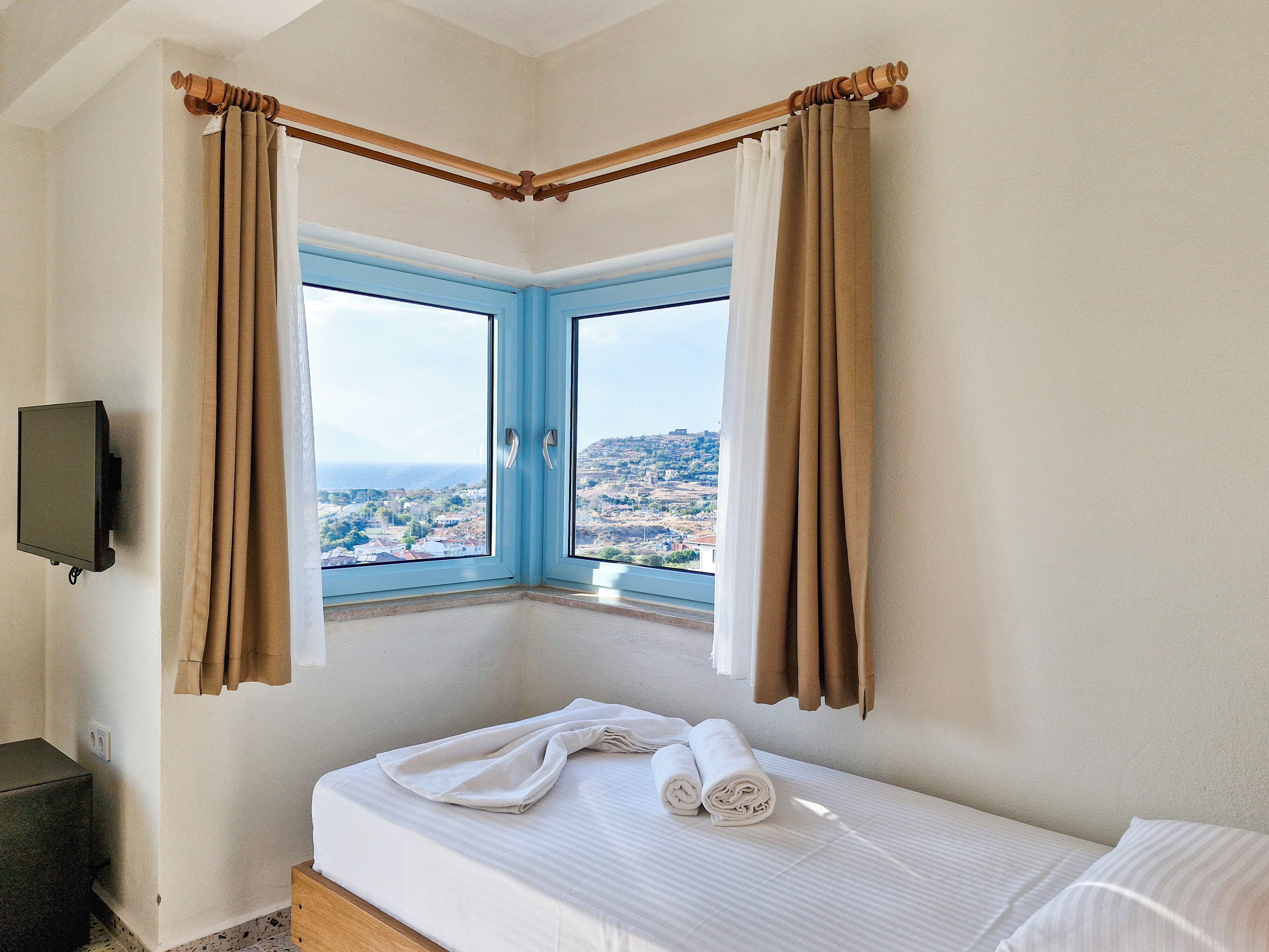 Una habitación de hotel con cama, televisión y ventana con cortinas.