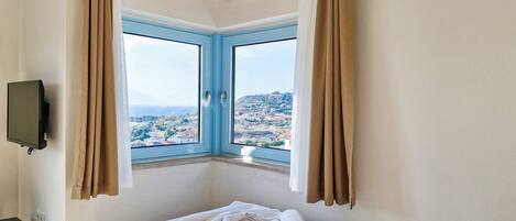 Una habitación de hotel con cama, televisión y ventana con cortinas.
