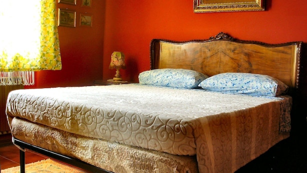 Una cama con cabecera de madera, dos almohadas y una colcha estampada.