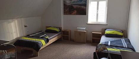 Une chambre de dortoir avec deux lits simples, un ventilateur de plafond, une fenêtre et un petit bureau.