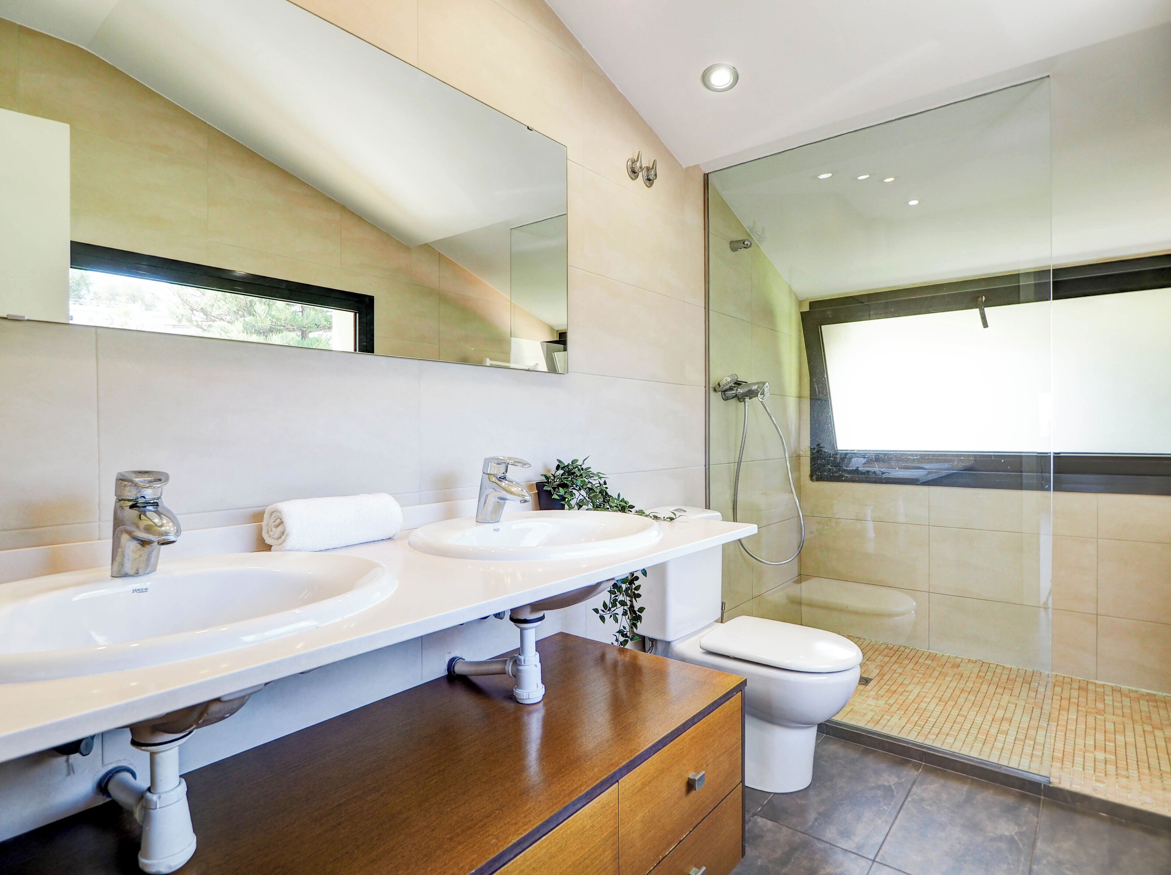 Een moderne badkamer met twee wastafels, een toilet en een douche met glazen wand.