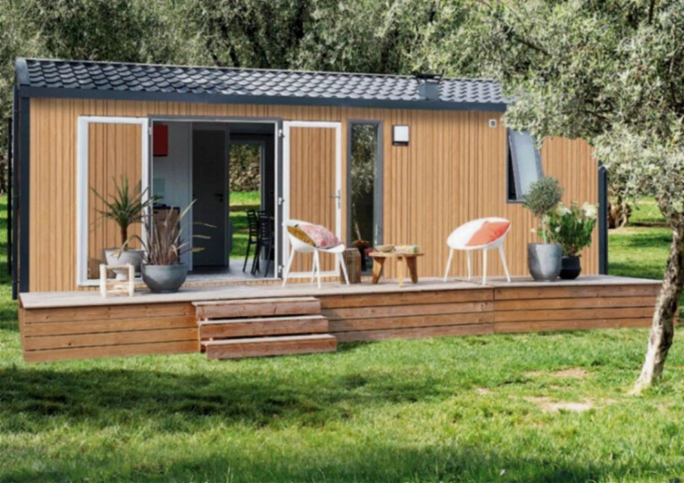 Une cabane moderne en bois, de plain-pied, avec un toit en tuiles, une véranda dotée de deux chaises et une petite table.
