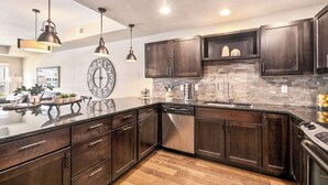 A modern kitchen with dark wood cabinets, a stainless steel dishwasher, and a large clock on the wall. - Old Town North Getaway – King Beds & Game Room! (Fort Collins)