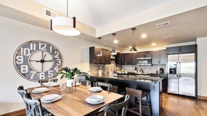A modern kitchen with a central island, stainless steel appliances, and a large wall clock. - Old Town North Getaway – King Beds & Game Room! (Fort Collins)