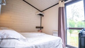 A bedroom with a bed, a window with curtains, a radiator, and a wall-mounted shelf. - ZEcamping 4 étoiles piscine chauffée chalet TV LV BBQ 35m2 (Aramits)