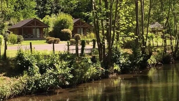 A serene lakeside setting with wooden cabins and lush greenery. - ZEcamping 4 étoiles piscine chauffée chalet TV LV BBQ 35m2 (Aramits)