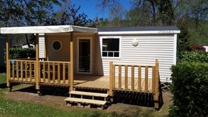 Ein kleines, eingeschossiges Mobilheim mit einer Holzterrasse und einer überdachten Veranda.