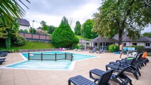 Ein Schwimmbecken mit Holzterrasse, Liegestühlen und einer überdachten Lounge-Ecke.