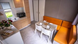 Eine kompakte Küche mit einer Mikrowelle, einem Spülbecken und Holzschränken. Es gibt einen Essbereich mit einem Tisch für zwei Personen und einer orangefarbenen Bank.
