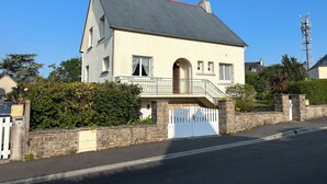 Une maison à deux étages dotée d’un balcon, d’un mur en pierre et d’une entrée fermée par un portail.