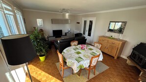 Un coin repas avec une table dressée pour quatre personnes, une plante en pot et un téléviseur en arrière-plan.
