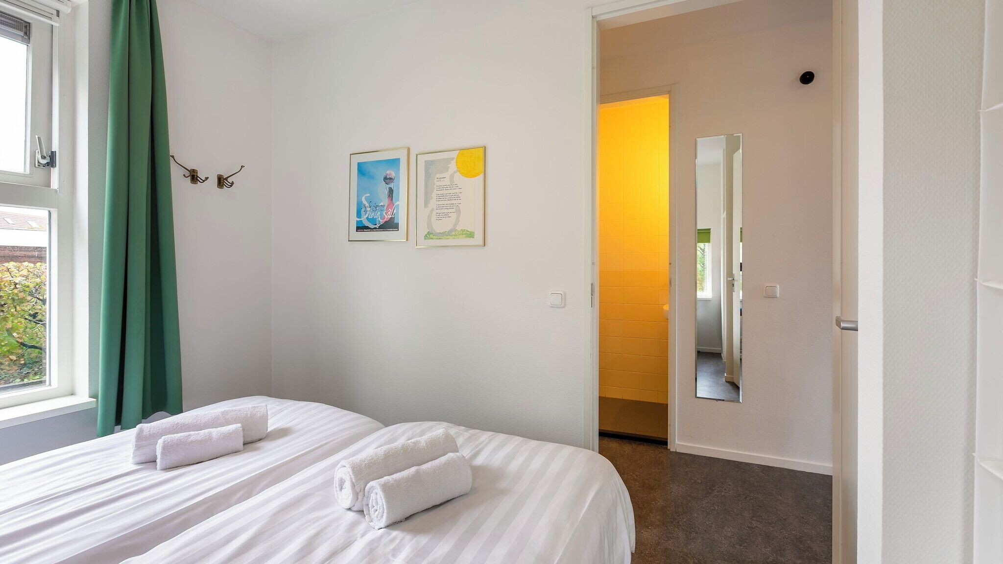 Una habitación de hotel con dos camas, una ventana con cortinas verdes y dos cuadros en la pared.