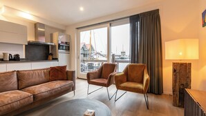 A modern living room with a sofa, two armchairs, a coffee table, a lamp, and a view of the harbor. - Summio Havenresort Terherne (Terherne)