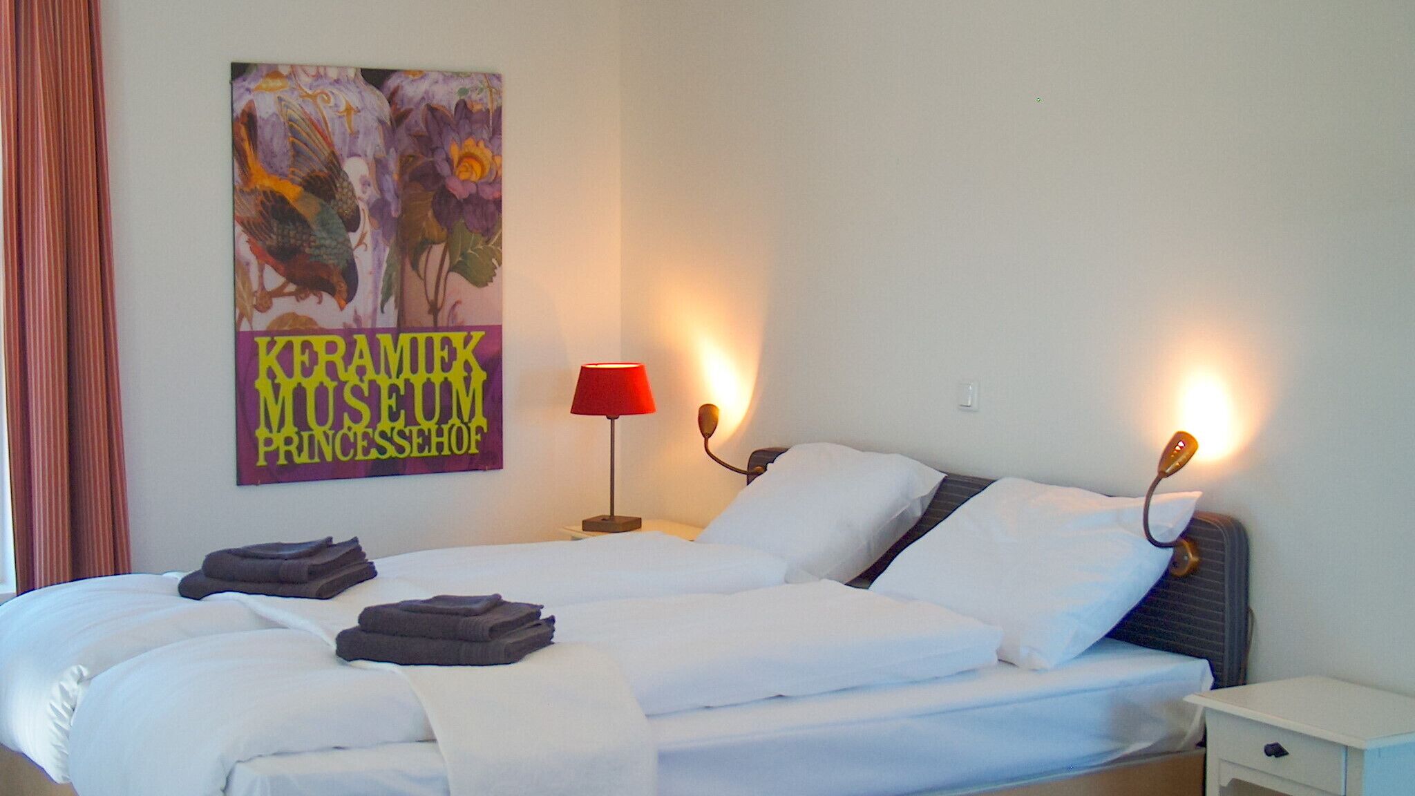 A hotel room with a bed, two bedside lamps, a nightstand, and a poster on the wall.