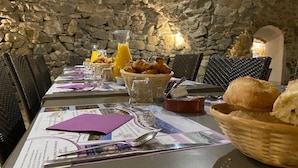 A breakfast setting with a stone wall backdrop, featuring croissants, bread, and orange juice on a table with menus and cutlery. - ZEcamping 4* familial piscine chauffée locatif clim 15m2 (Rosans)