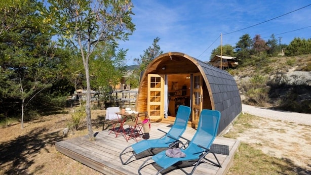 A wooden cabin with a curved roof, a deck with lounge chairs, and a table. - ZEcamping 4* familial piscine chauffée locatif clim 15m2 (Rosans)