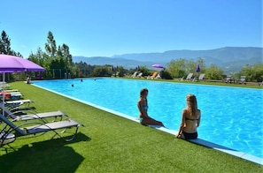 Una piscina amb vista a muntanyes, envoltada d'herba i gandules.