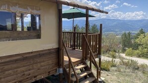 Une terrasse en bois avec un escalier menant à une zone abritée, d’où l’on peut admirer un paysage montagneux.