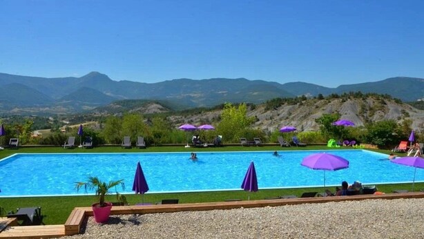 Une piscine dotée de plusieurs couloirs, entourée de chaises longues et de parasols, avec une chaîne de montagnes en toile de fond.