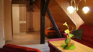 Et hyggeligt rum med træloft, en rød sofa, et træbord med en vase og en trappe i baggrunden.