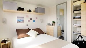 Ein Hotelzimmer mit Bett, Nachttisch, Kleiderschrank und kleinem Schreibtisch mit Pflanze.