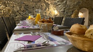 Ein Frühstückstisch mit Blick auf eine Steinsandsteinmauer, mit Croissants, Brot und Orangensaft, Menüs und Besteck.