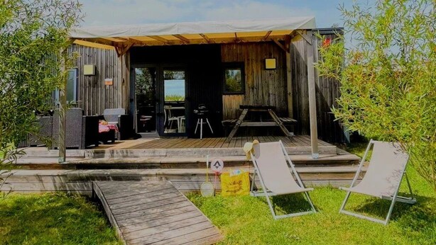 Una cabaña de madera rústica con un porche cubierto, mobiliario exterior y una pequeña terraza.
